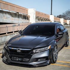 the front end of a black car parked in a parking lot next to a bridge