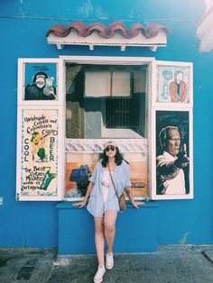 a woman standing in front of a blue building with posters on the wall behind her