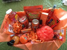 an orange basket filled with snacks and condiments on top of a green bedspread