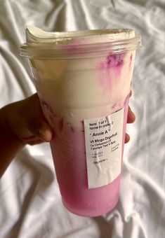 a person holding up a plastic cup with pink liquid in it on a white sheet