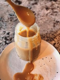 a spoon pouring caramel sauce into a jar on a white plate with black speckles