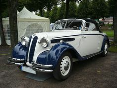 an old blue and white car parked in a parking lot next to a tented area