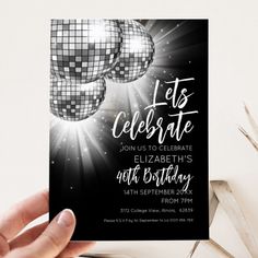 a person holding up a black and white party card with disco balls in the background