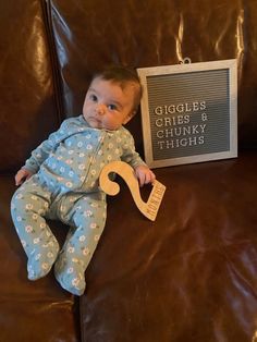 a baby sitting on top of a brown couch next to a sign that says giggles gries and chunky thighs