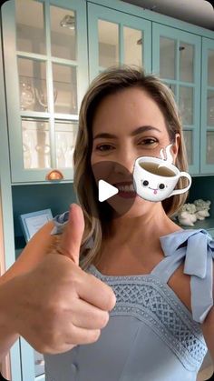 a woman is holding up a coffee cup in front of her face and giving the thumbs up