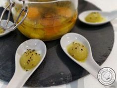 three spoons filled with liquid sitting on top of a black stone plate next to two jars