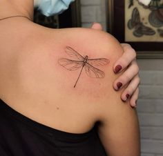 a woman's shoulder with a dragonfly tattoo on it