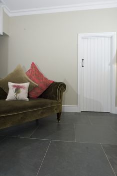 a brown couch sitting on top of a stone floor next to a white door in a living room