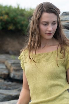 a woman in a yellow shirt is holding a cell phone and looking down at the ground