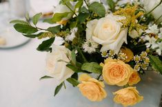 Image shows a zoomed in look at a white, yellow and green wedding reception centerpiece with white and yellow roses, chamomile, ruscus. Yellow Roses