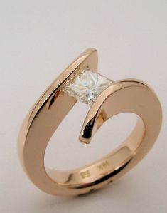 a gold ring with a princess cut diamond in the center, on a white background