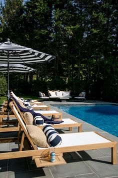 a row of lounge chairs sitting next to a swimming pool with an umbrella over it