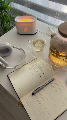 an open book sitting on top of a table next to a cup of tea and headphones