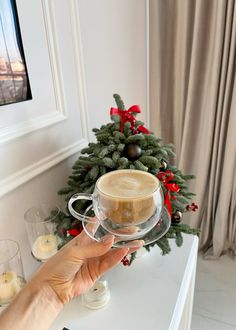 a person holding a cup of coffee in front of a christmas tree