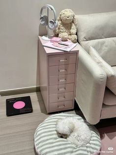 a white teddy bear sitting on top of a bed next to a pink dresser and chair