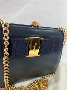 You are looking at a genuine dark navy blue leather Salvatore Ferragamo chain link shoulder bag. Measurements are 6"3 wide, 5" high, 1"7 deep with a  46" chain link shoulder strap with a 22" drop. On the interior there is one main compartment lined in black fabric, gold tone hardware , signature logo hardware along a lovely bow on the front with signature logo. Nice very hard to find mini chain bag that can also be used crossbody if petite. The interior was cleaned as the inner vinyl lining rubb Mini Chain Bag, Bag Measurements, Work Bag, Chain Bag, Dark Navy Blue, Chain Bags, Signature Logo, Blue Leather, Dark Navy