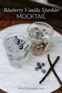 two glasses filled with ice and blueberries on a marble plate