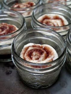 small glass jars filled with food sitting on top of a metal counter topped with cinnamon rolls