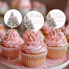 cupcakes with pink frosting and christmas trees on top are sitting on a cake plate