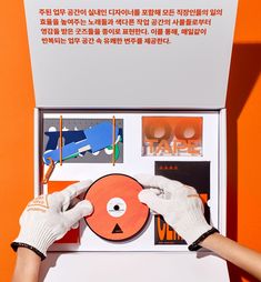 two hands in white gloves hold up a record with an orange disc on the cover