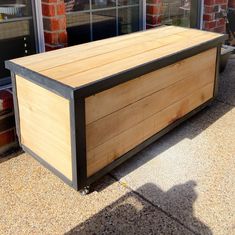 a wooden box sitting on top of a sidewalk next to a brick building with windows