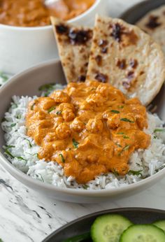 a bowl filled with rice covered in sauce next to cucumbers and pita bread