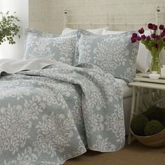 a bed with blue and white bedspread next to a vase filled with flowers