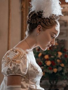 a woman wearing a white dress and feathered headpiece in front of a christmas tree