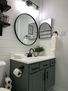 a white toilet sitting next to a bathroom sink under a round mirror on top of a wall