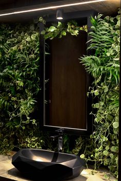 a bathroom sink sitting under a mirror in front of a wall covered with green plants