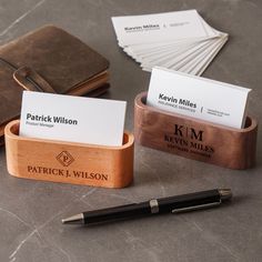 two business cards in a wooden holder with a pen on the table next to them