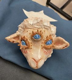 a ceramic sheep head with blue eyes on top of a tablecloth covered chair cushion