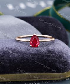 a gold ring with a red stone on the front and side, sitting on top of a velvet cushion