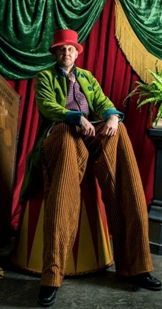 a man sitting on top of a chair in front of a red and yellow curtain