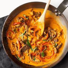 a skillet filled with meat and vegetables on top of a black cloth next to a wooden spoon