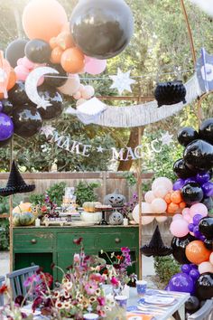 an outdoor party with black, white and orange balloons hanging from the ceiling over a table