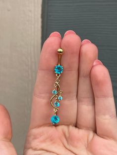 a person is holding a gold and blue jeweled navel bar in their left hand