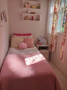 a small bedroom with pink bedding and curtains on the window sill above it