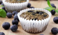 two blueberry muffins sitting on top of a wooden table next to fresh blueberries