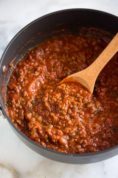 a wooden spoon in a pot full of chili sauce on a marble counter top,