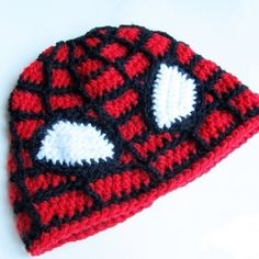 a crocheted red and black beanie hat with white hearts on it sitting on a table