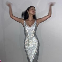 a woman in a silver sequin dress with her arms up and hands out to the side