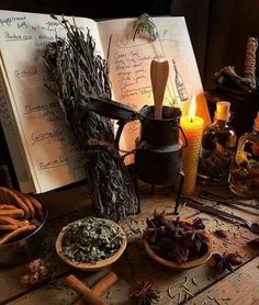 an open book sitting on top of a wooden table next to bowls filled with herbs