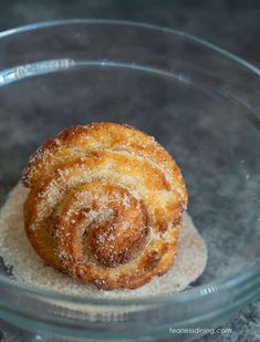 a cinnamon roll in a glass bowl with sugar on the bottom and powdered sugar on top