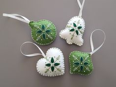 three green and white ornaments are hanging on a gray surface, with ribbons in the shape of hearts