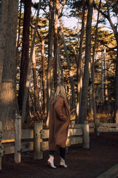 a woman is walking through the woods with her coat over her shoulders and white shoes on