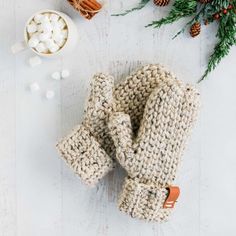 two knitted mittens sitting on top of a table next to marshmallows