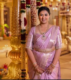 a woman in a pink sari standing next to some gold pillars and flower garlands