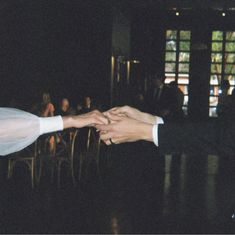 two people holding hands in front of a group of people sitting at tables and chairs