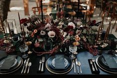 the table is set with black plates, silverware and red floral centerpieces